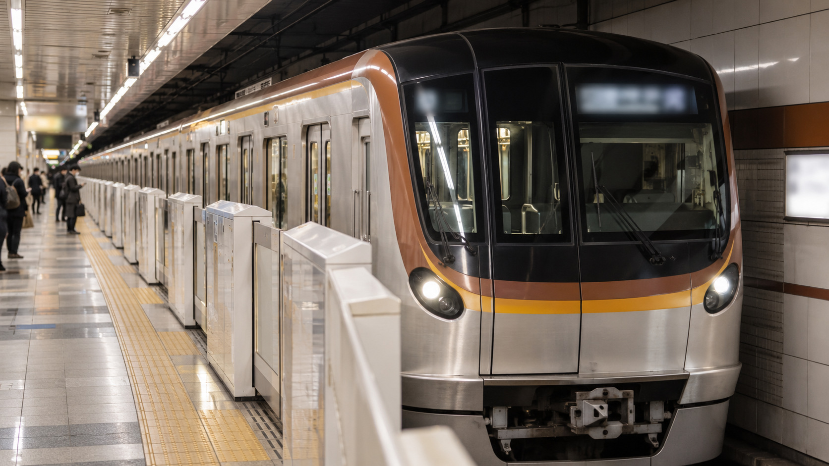 A silver, ochre and brown Fukutoshin Line-style train stands behind platform doors.