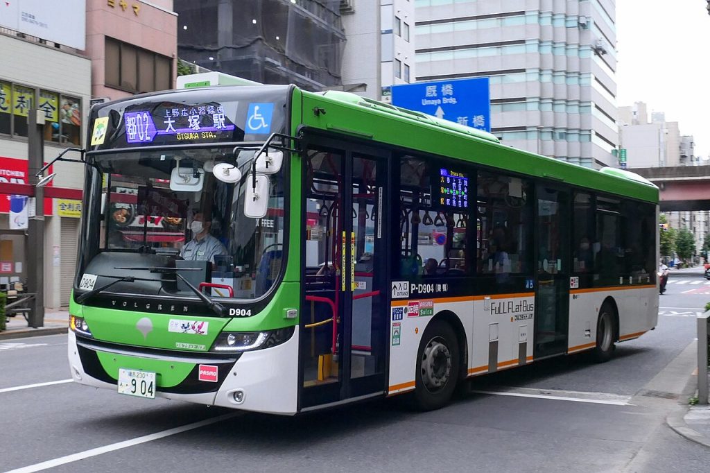 A green and white Toei city bus seen from the front-left side in Tokyo.